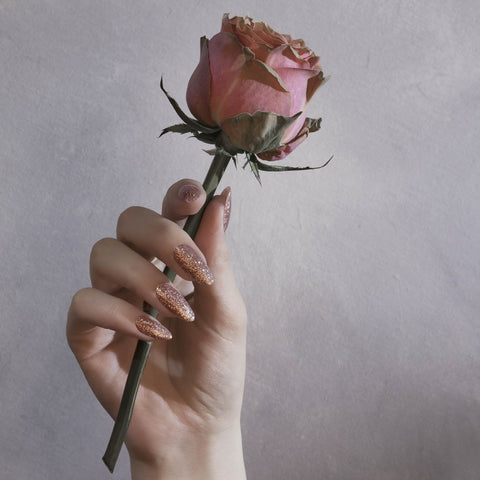 Rose gold glitter manicure holding flower